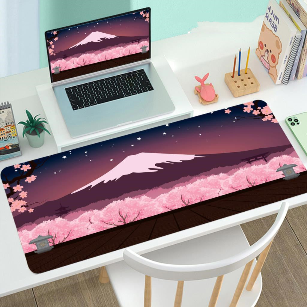 Laptop on a desk with a large mouse pad featuring a mountain and cherry blossom design.